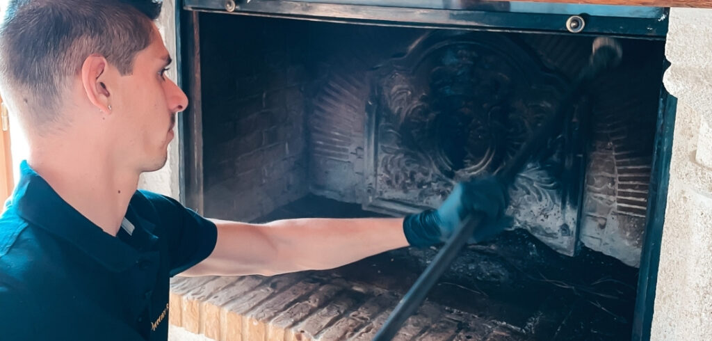 Ramoneur nettoyant l’intérieur encrassé d’une cheminée avec un outil de ramonage, portant des gants de protection.